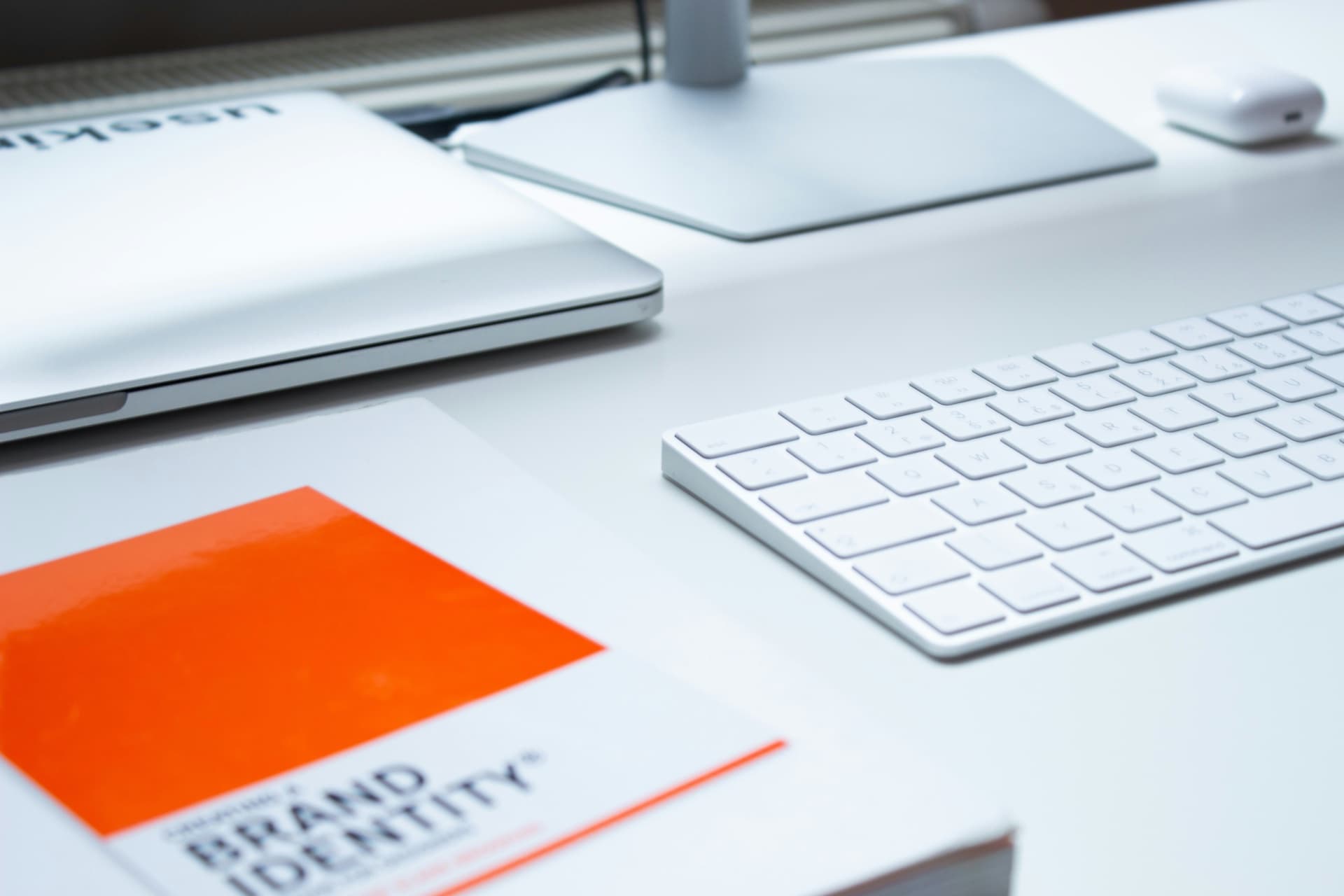 Ein modernes Büroset auf einem hellgrauen Schreibtisch, komplett mit einem MacBook, einer Tastatur und einem farbenfrohen orangefarbenen Ordner, sorgt für eine produktive Arbeitsumgebung. Diese minimalistische Büroeinrichtung, wie auf dem Bild image_de186a.jpg zu sehen ist, kombiniert Stil und Funktionalität für eine inspirierende Arbeitsumgebung.