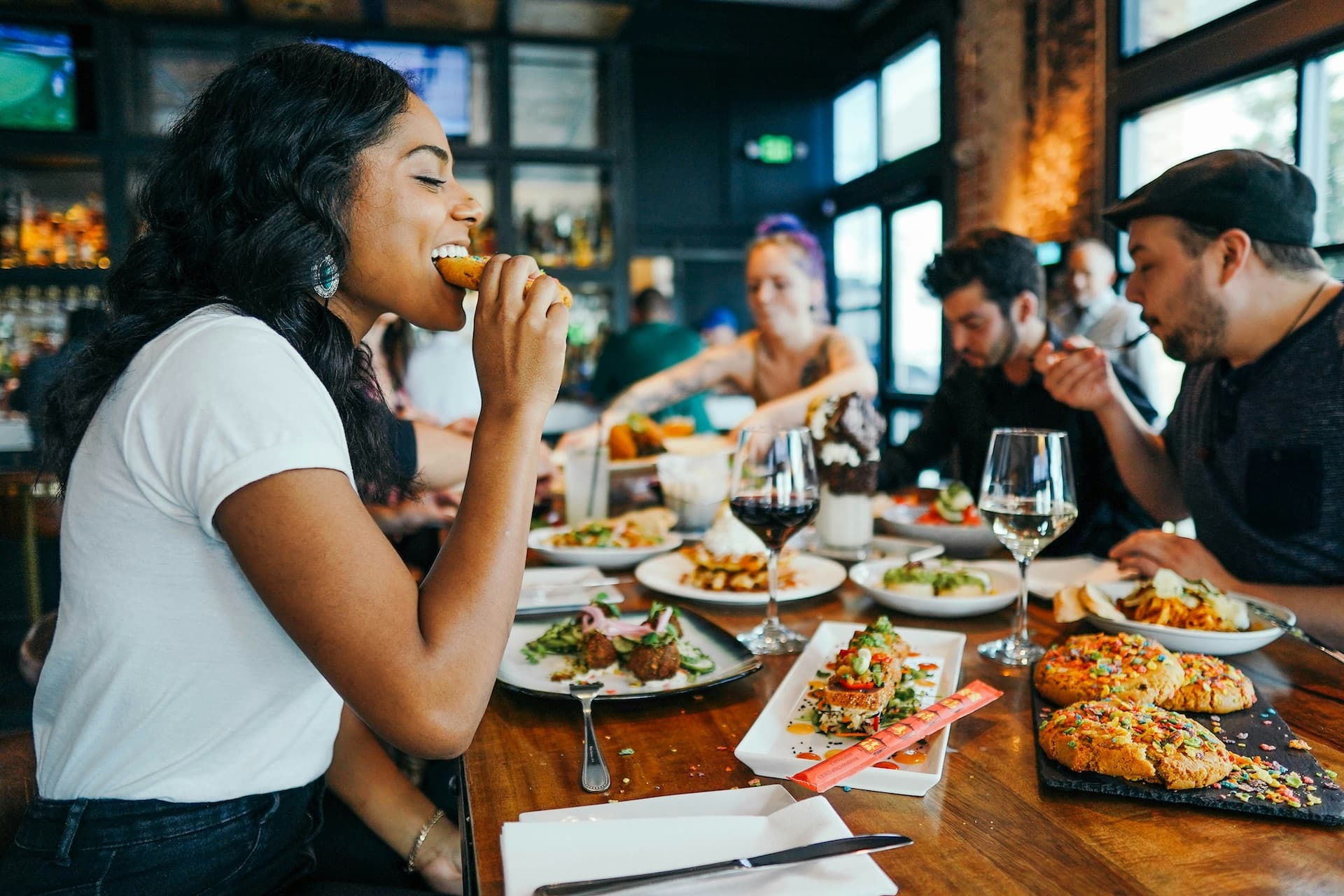 Freunde genießen gemeinsam ein vielseitiges Essen in einem modernen Restaurant mit Wein und verschiedenen Gerichten.